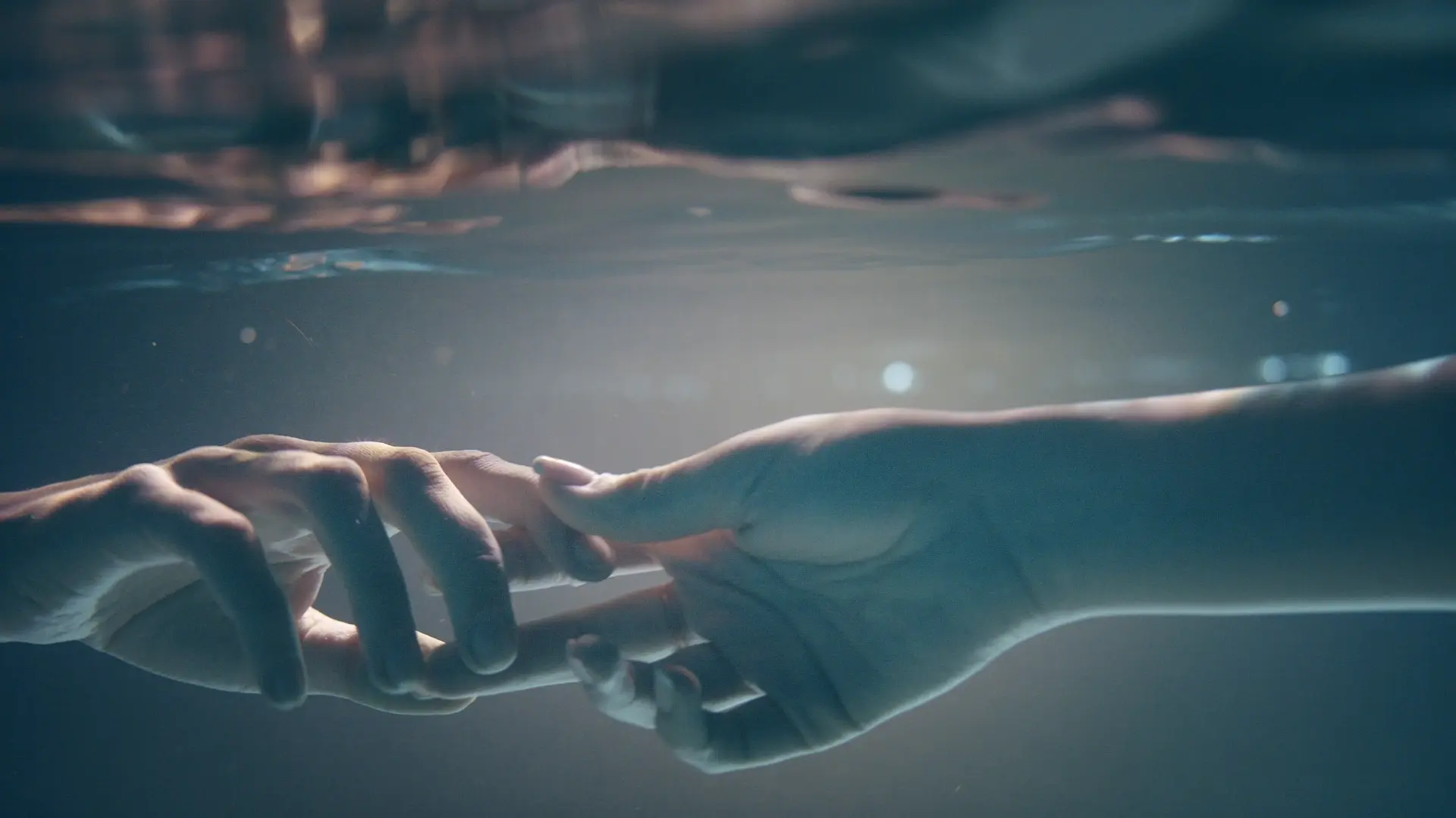 Manos tocándose suavemente bajo el agua, simbolizando la alquimia del contacto